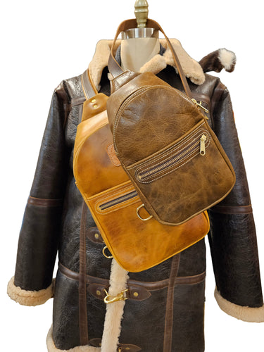 A brown leather sling bag displayed on a mannequin wearing a black jacket.