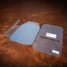 A set of clear acrylic templates used for creating a flex sling bag made from leather. Laid against a textured brown leather background