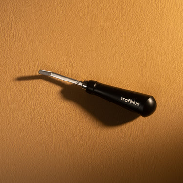 A stainless steel roughing tool used for texturing leather textiles and projects. Laid out on a light brown textured leather background.