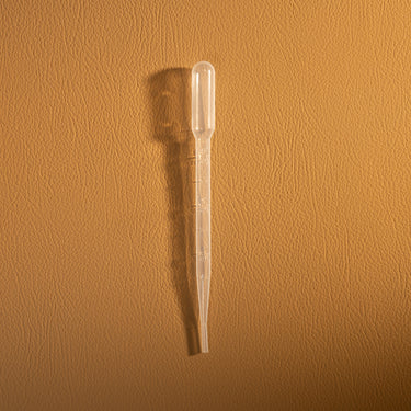 Clear plastic pipette on a brown textured background
