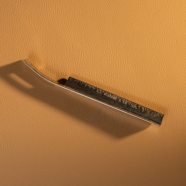 A replacement metal blade for a skiving knife, which is used for leather projects and crafting. Laid out on a brown textured leather background.