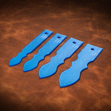 A set of blue acrylic templates used for creating custom strap ends in a western style for belts. Laid out on a textured brown leather background.