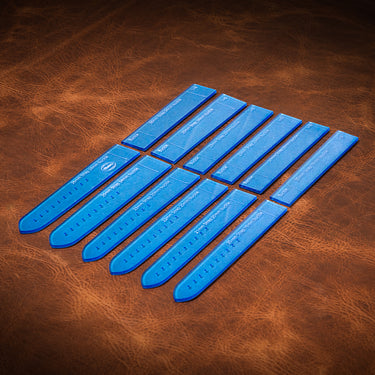 A set of blue acrylic templates used for creating custom watch bands made from leather. Laid out on a brown textured leather background.