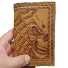 A hand holding a small brown leather notebook with a skull and web pattern.